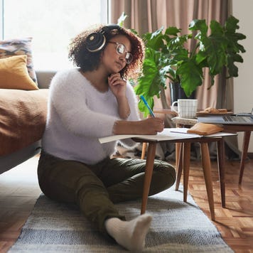 Young woman sitting in living room while working on laptop with headphones on