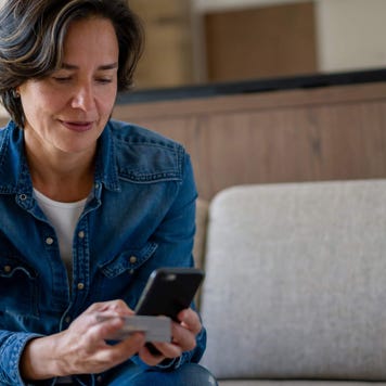 Middle-aged woman uses her phone while holding her credit card at home