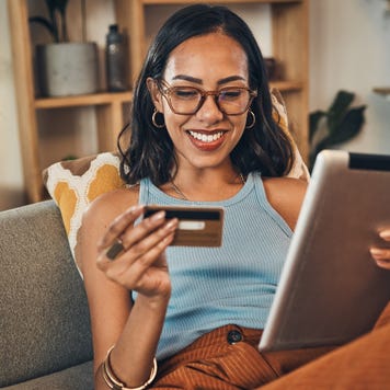 Smiling woman using credit card for ecommerce on digital tablet at home