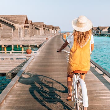 Young woman riding bicycle on wooden pier in the Maldives