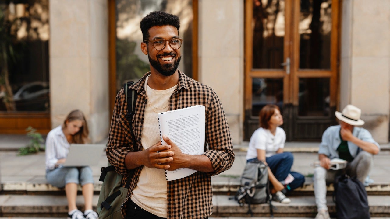 Man stands outside college building with papers