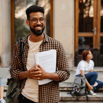 Man stands outside college building with papers