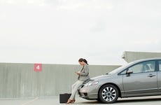 Business woman texting while leaning on the hood of her silver sedan in a car park