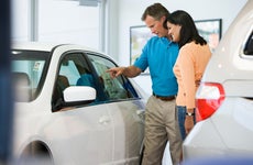 Man and woman browsing white car's sticker price in dealership