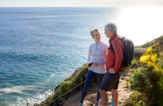 Couple talking while standing on cliff by sea during sunny day