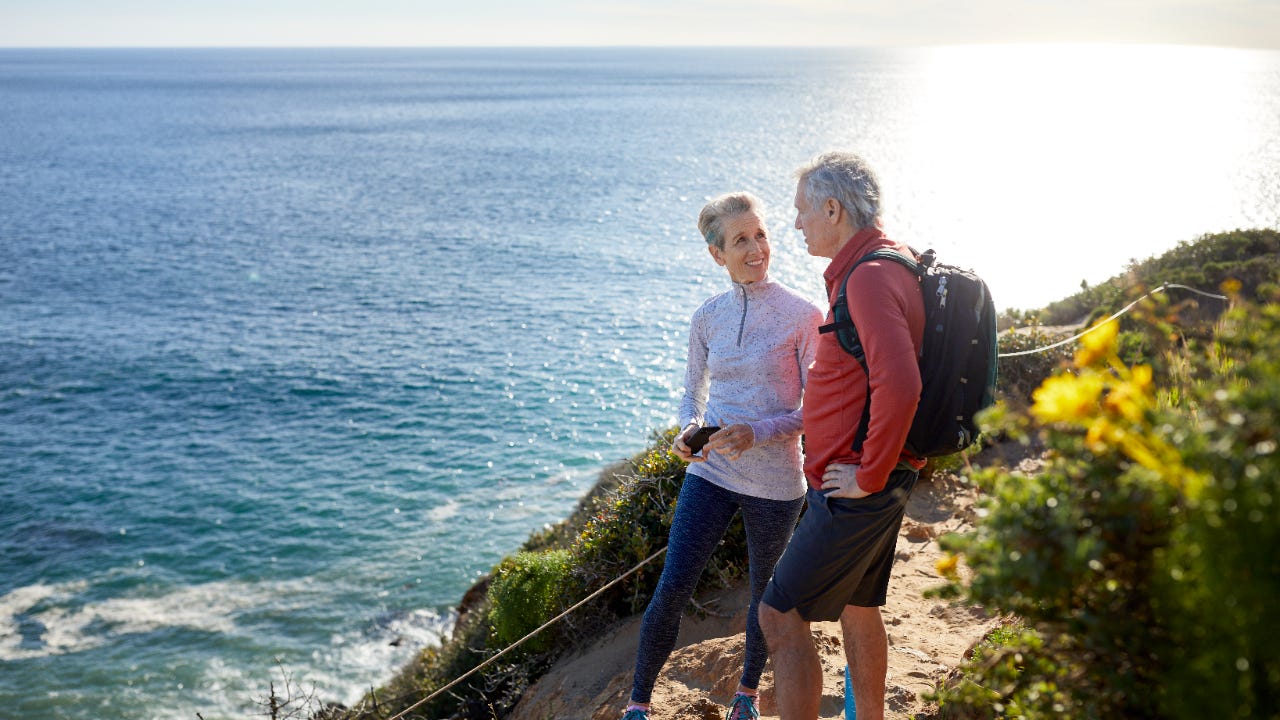 Couple talking while standing on cliff by sea during sunny day