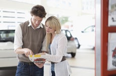 Man and woman in car showroom in front of white car looking at brochures
