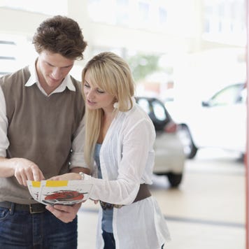 Man and woman in car showroom in front of white car looking at brochures