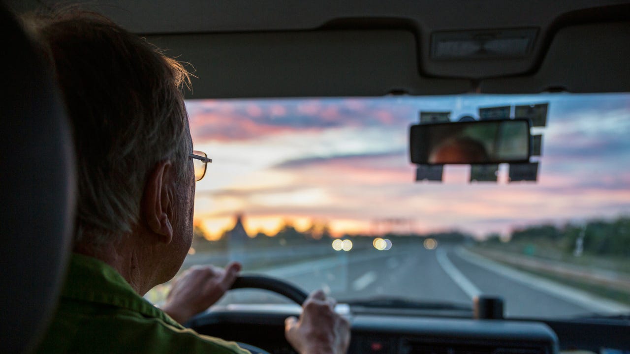 Senior man driving a car on a highway at sunset