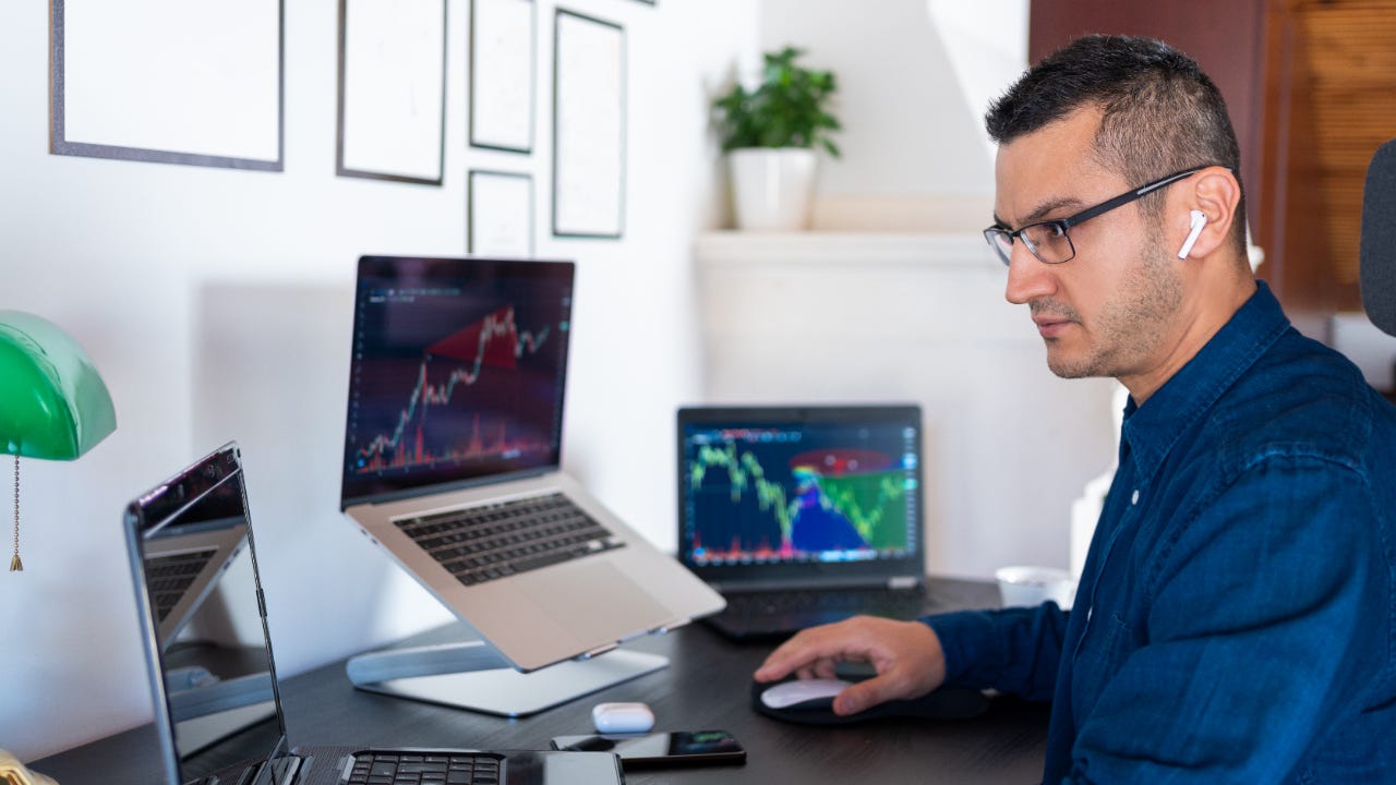 A trader sits at his desk and trades on his laptop computers