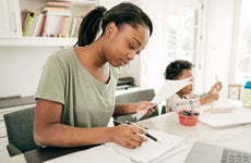 Mom preparing financial paperwork at home while her child draws next to her