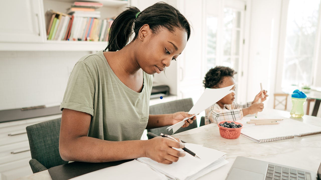 Mom preparing financial paperwork at home while her child draws next to her