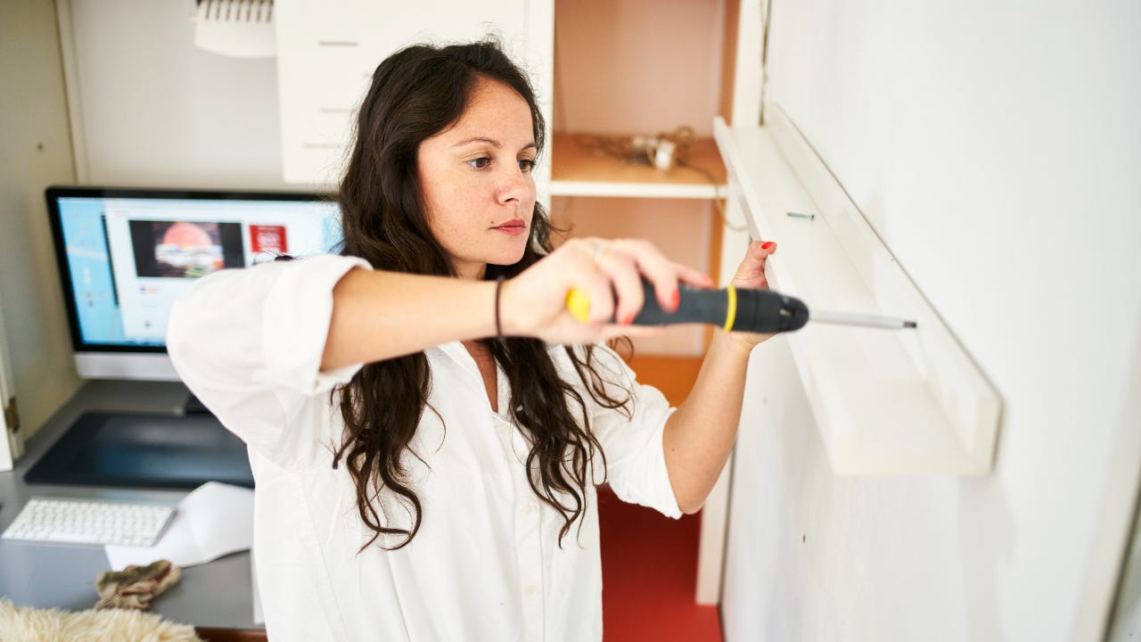 woman fixing a shelf at home with a screwdriver