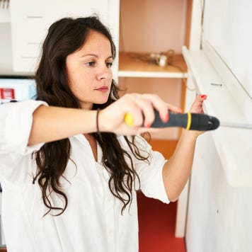 woman fixing a shelf at home with a screwdriver