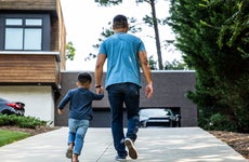 Rear view of a father walking up driveway with his young son