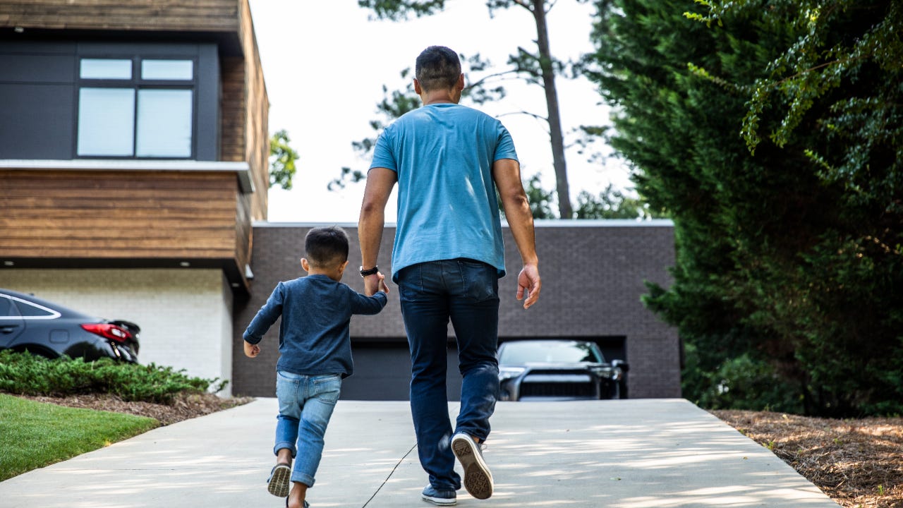 Rear view of a father walking up driveway with his young son