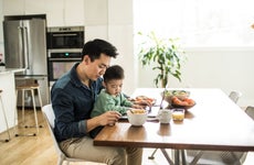 Father multi-tasking with young son at kitchen table