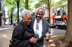An older couple laughs as they walk down a city street