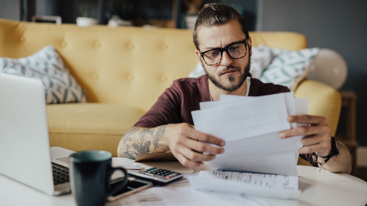 man working on his finances at home with laptop and papers