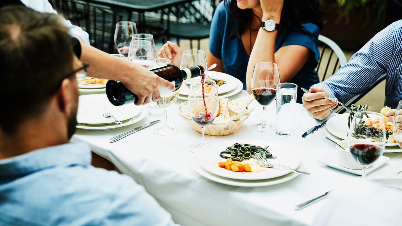 Server pouring wine for friends having a meal on restaurant patio