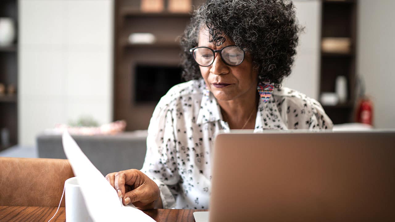 senior woman looking at paperwork in front of a computer