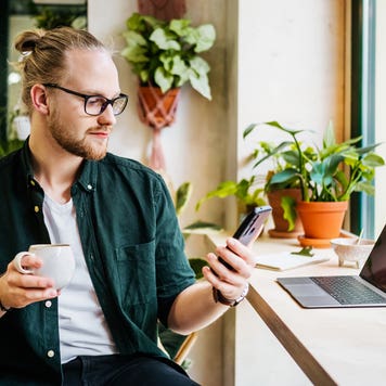 man looking at phone while having coffee in cafe