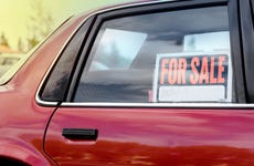 A close up of the back passenger side window of a red car with a for sale sign in the window