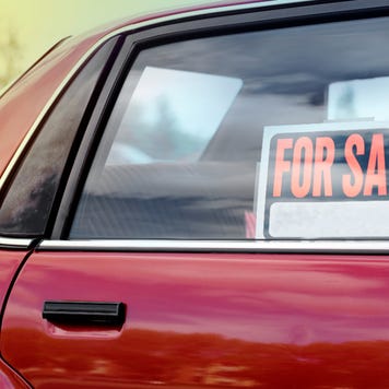 A close up of the back passenger side window of a red car with a for sale sign in the window