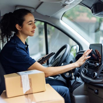 Woman in driver seat of vehicle using touch screen on dash with two packages in passenger seat
