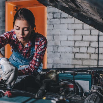 Female mechanic working on engine in a brick garage