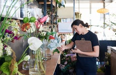 florist talking on the phone with a customer and carrying a clipboard while working in her flower shop