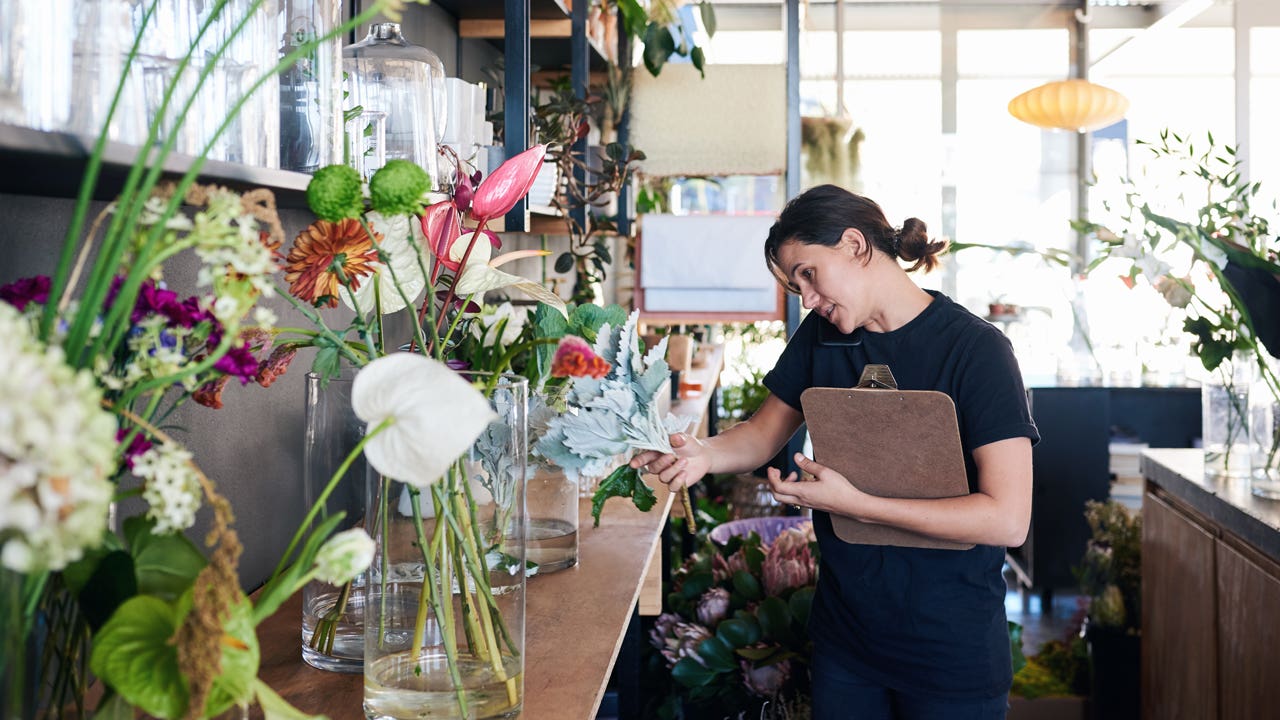florist talking on the phone with a customer and carrying a clipboard while working in her flower shop