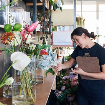 florist talking on the phone with a customer and carrying a clipboard while working in her flower shop