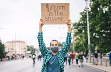 A man holds a cardboard sign that says Bitcoin is the answer