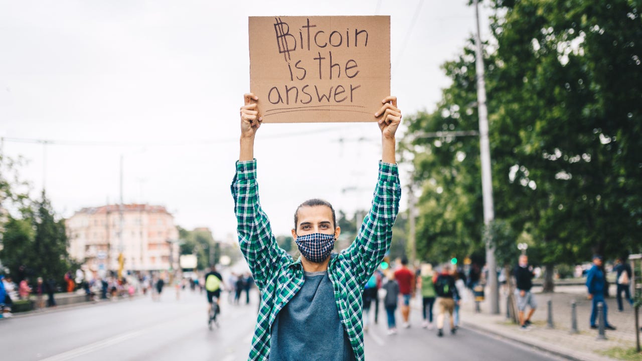 A man holds a cardboard sign that says Bitcoin is the answer