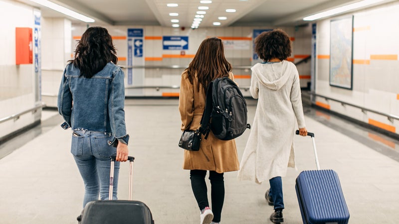 three women walking in airport hallway with luggage