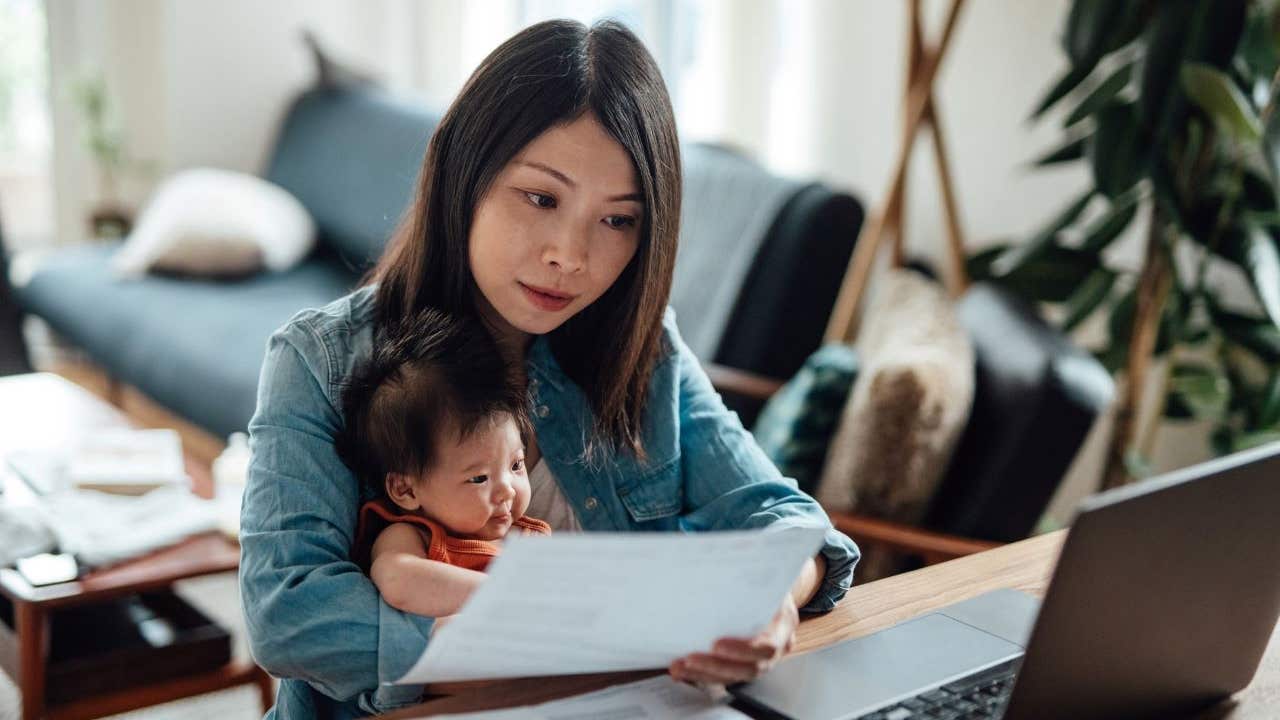Woman holding her baby while analyzing her finances