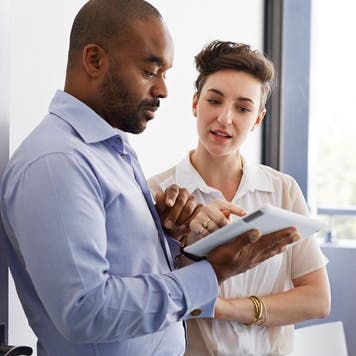 Black man and white woman look at a tablet together.