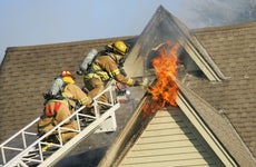 two firefighters on a ladder working to put out a house fire