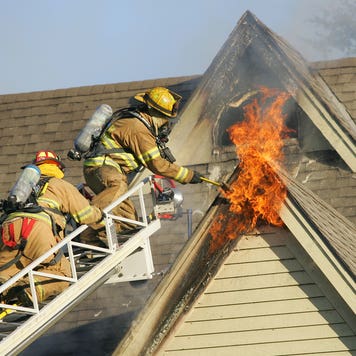 two firefighters on a ladder working to put out a house fire