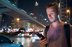 Illuminated face of young man during using mobile phone on busy city street at night.