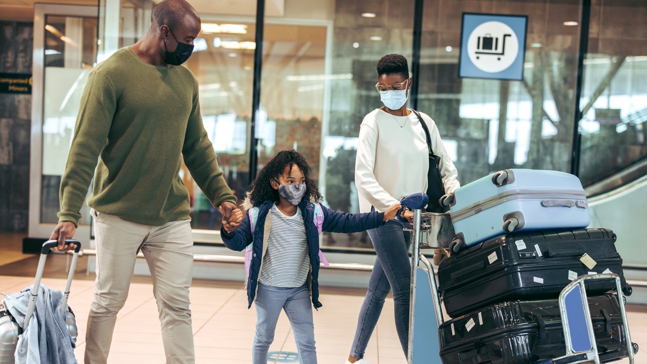 family of three walking through airport with luggage