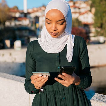 woman looking at smart phone while holding credit card