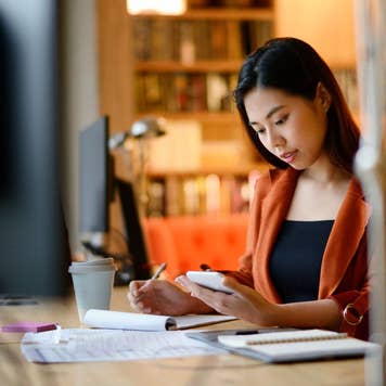woman writing in notebook and looking at her phone
