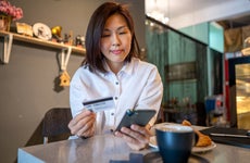 woman using smartphone and credit card while sitting in cafe