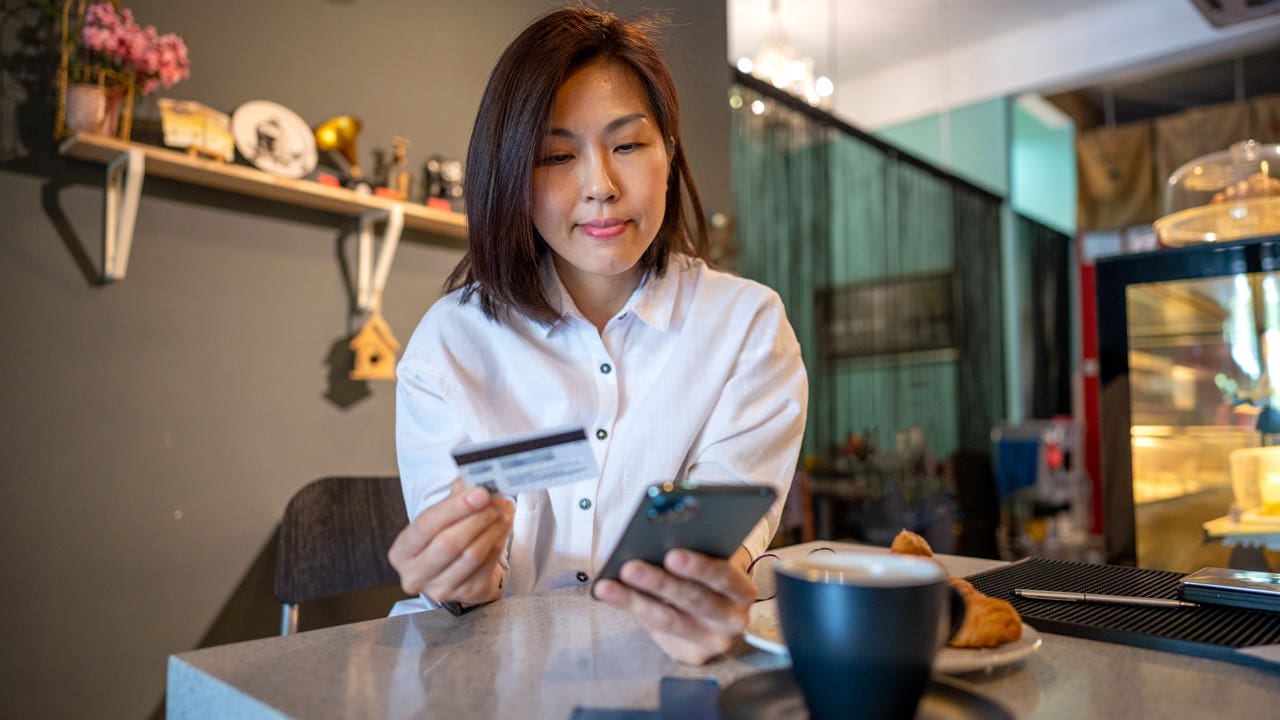 woman using smartphone and credit card while sitting in cafe