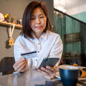 woman using smartphone and credit card while sitting in cafe