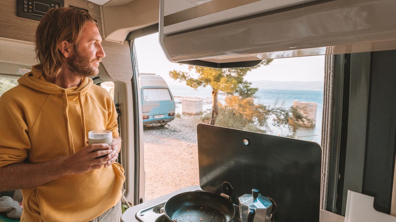Man drinks coffee in his van, sea view
