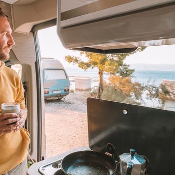 Man drinks coffee in his van, sea view