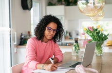 Multiracial woman having home office in kitchen, writing notes.